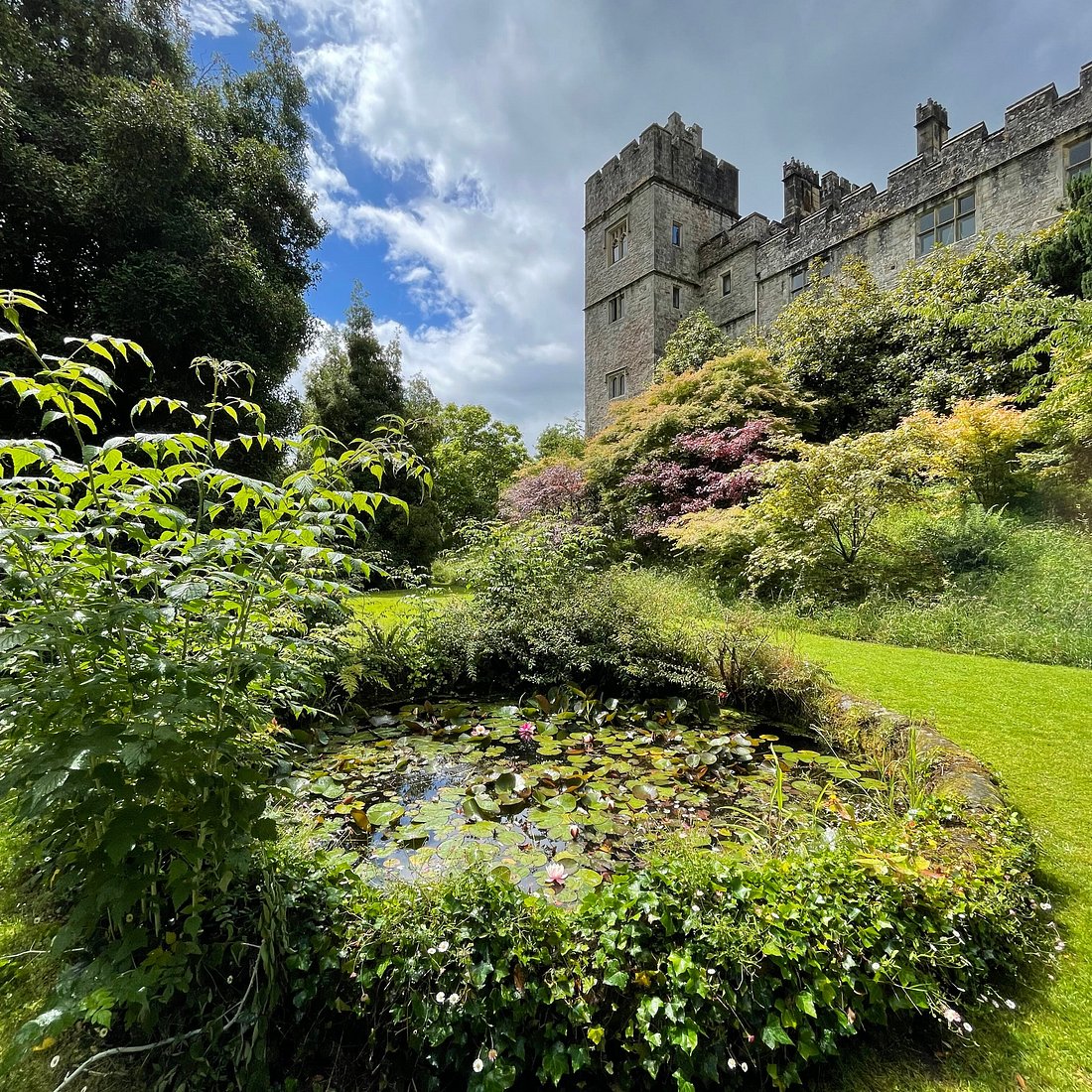 Medieval castle on hillside above ornamental gardens with pond and colorful plants