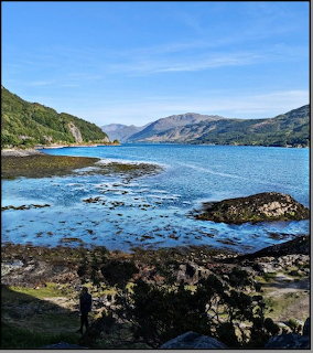 Loch Ness lake in Scotland surrounded by green hills under a bright summer sky