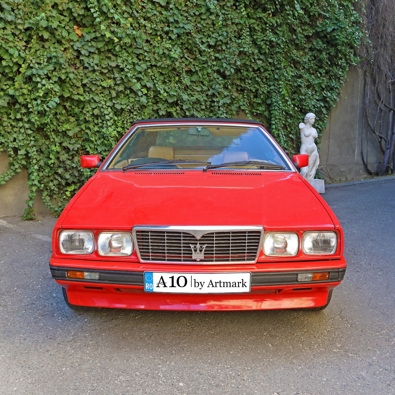 Red 1988 Maserati Bi Turbo Spyder convertible parked on driveway with ivy wall