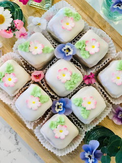Pastel iced petit fours with flower decorations arranged on a wooden tray
