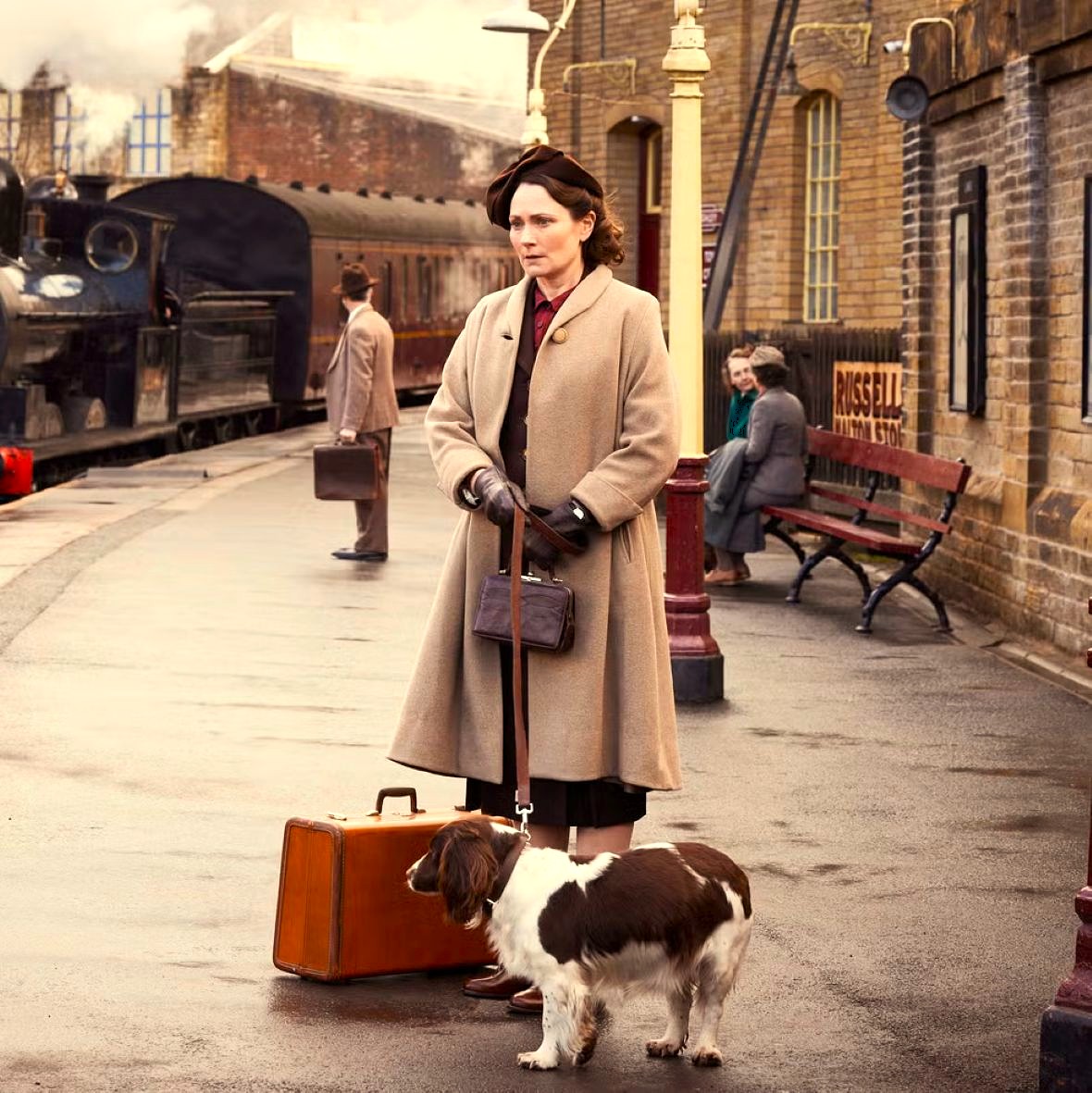 Woman with a dog and suitcase on a train station platform near a steam train