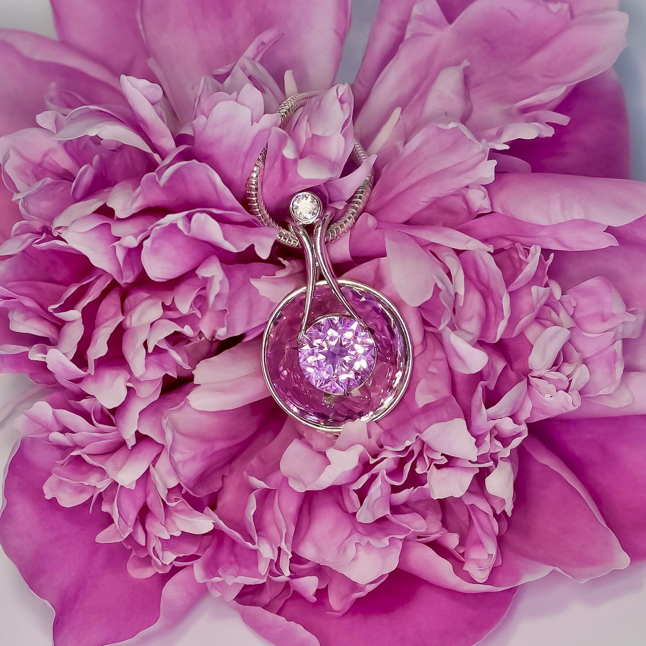 Close-up of a pink gemstone pendant resting on pink peony petals