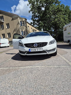 White Volvo sedan parked in a parking area with buildings and trees in the background