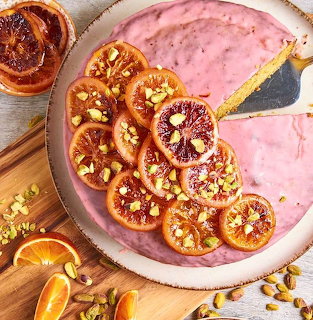 Pink iced cake topped with blood orange slices and pistachios on a wooden board