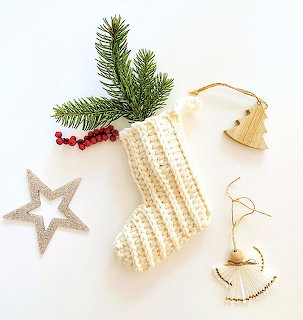 Handmade Christmas ornaments with crocheted stocking, wooden decorations, and pine branch arranged on white surface