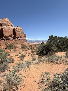 Red sandstone rock formation with desert brush and juniper trees at Arches National Park Utah