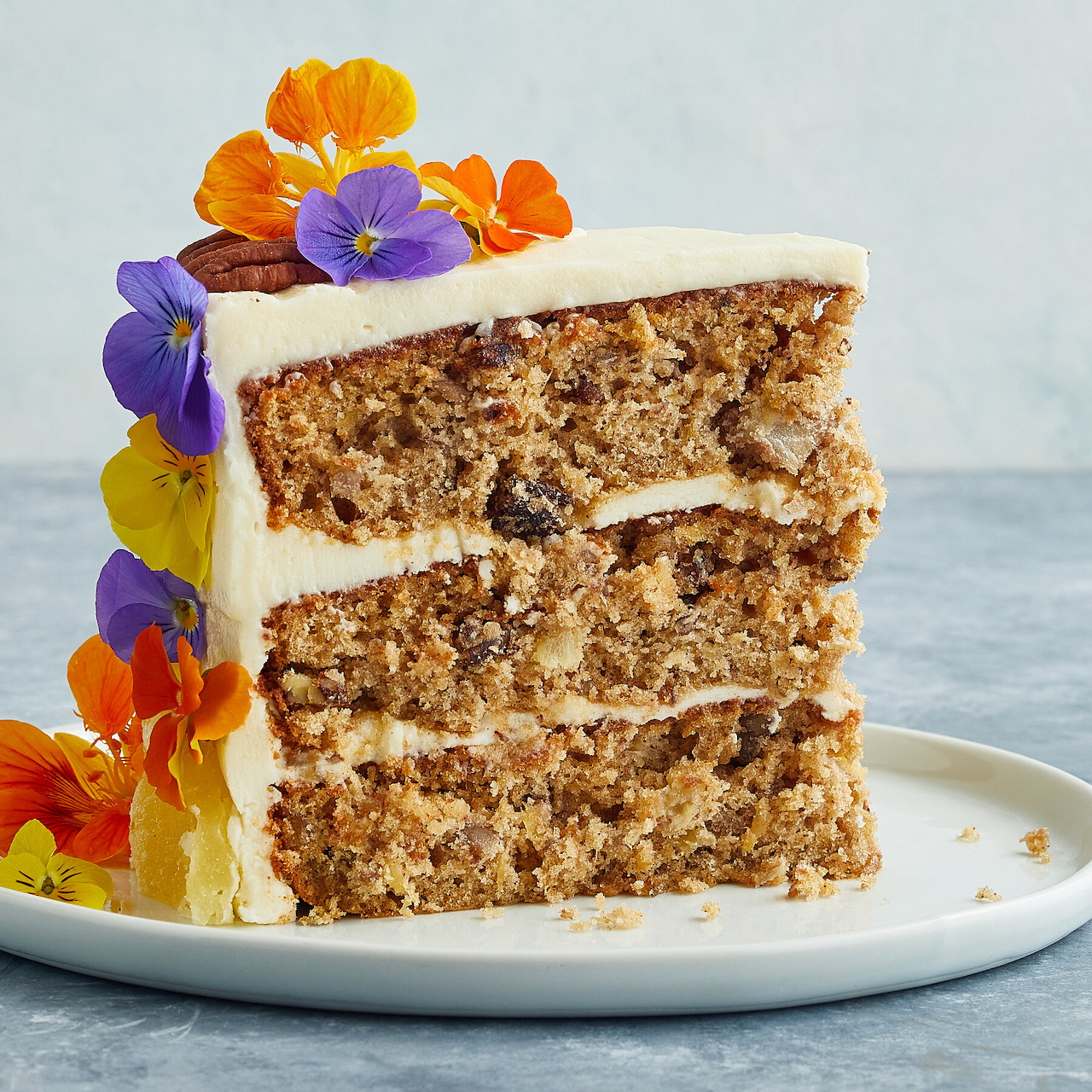 Three-layer spiced cake with white frosting and edible flowers on a white plate