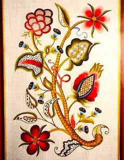 Crewel embroidery with colorful floral design featuring red flowers, gold vines, and decorative leaves on cream fabric