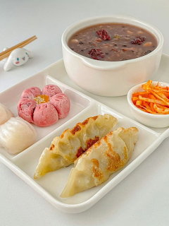 Korean dumplings, pink bun, red bean soup, kimchi and pickled radish on white compartment tray