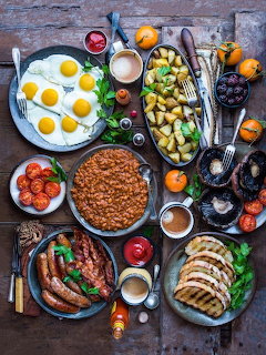 Overhead view of dinner table with eggs, sausages, roasted vegetables, and sliced meat on rustic wood