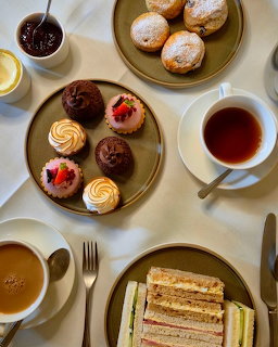 Overhead view of afternoon tea with pastries, sandwiches, and tea cups on marble table