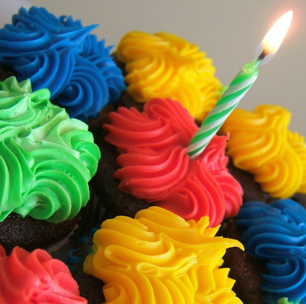 Colorful cupcakes with swirled frosting in bright colors and a single lit candle
