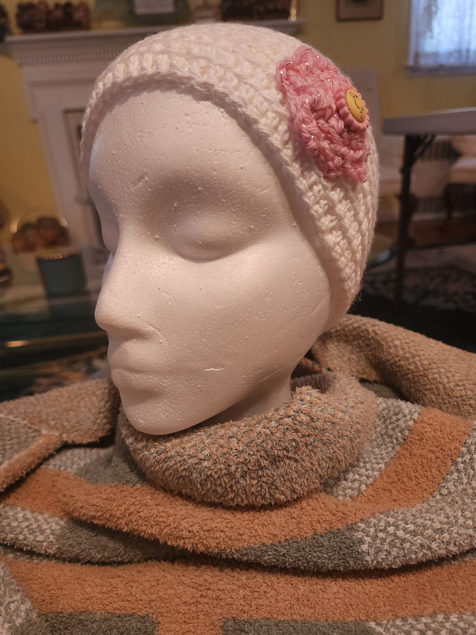 White mannequin head wearing a knitted hat with a flower and a thick striped scarf indoors