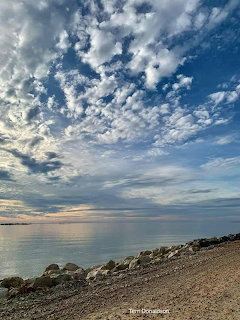 Rocky beach and calm sea beneath a dramatic cloudy sunset sky