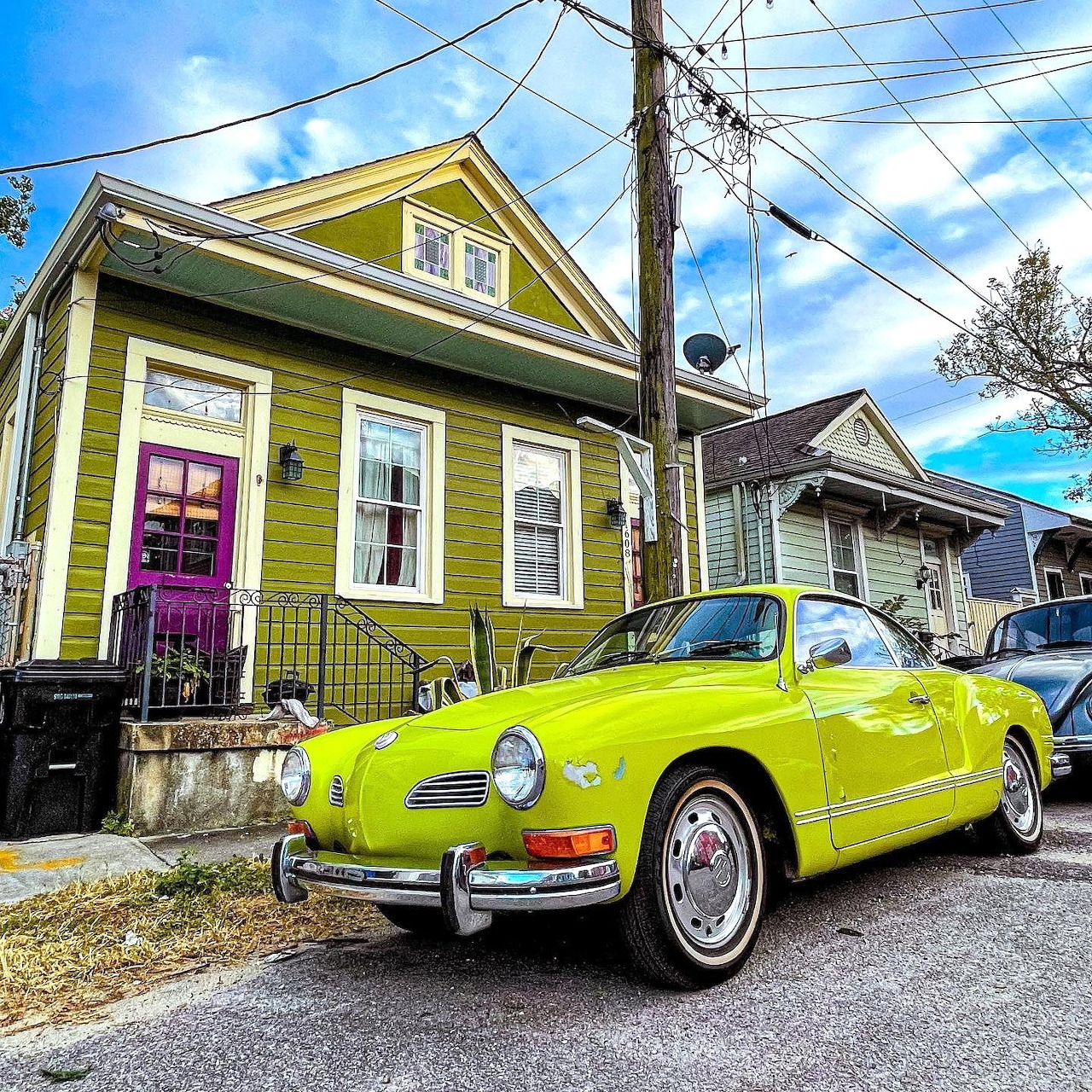 Lime green vintage car parked before a green house under blue sky