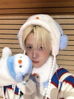 Young person in white fluffy winter hat holding a snowman stuffed toy indoors
