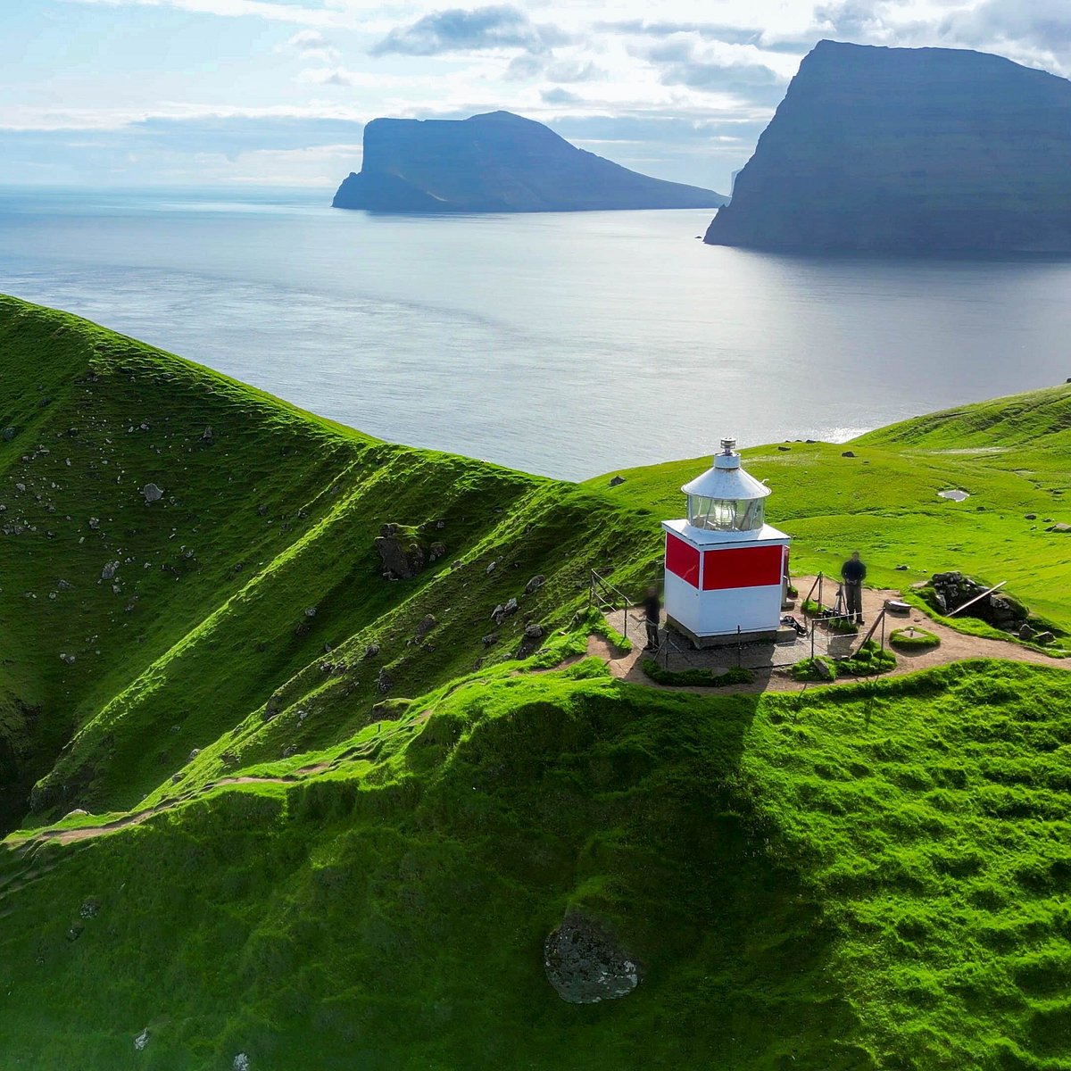 Red and white lighthouse on lush green cliffs with ocean and islands in background