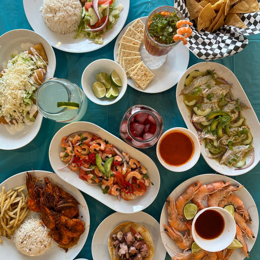 Overhead view of assorted seafood dishes, tacos, shrimp, rice, fries, vegetables, and sauces on a table
