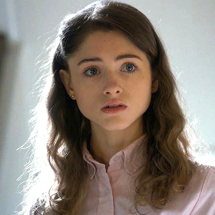 Portrait of Natalia Dyer with wavy brown hair wearing a pale pink blouse