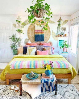 Bright boho bedroom with colorful bed linens, pillows, hanging plants, and woven wall decor
