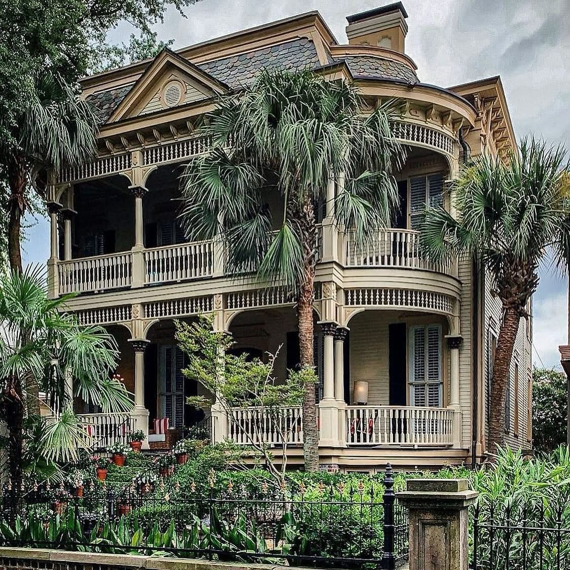 Three-story Victorian house with porches and palm trees in front garden