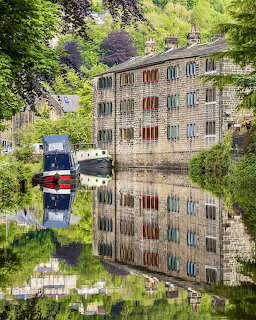 Stone buildings and a boat reflected in a calm canal under green trees
