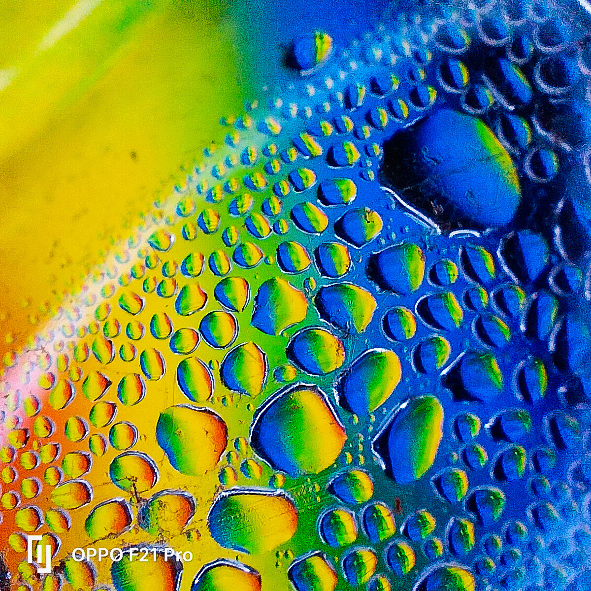 Close-up of water droplets on rainbow gradient surface showing yellow, green, and blue colors with light reflections
