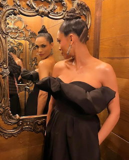 Woman in black off-shoulder dress standing by ornate gold mirror