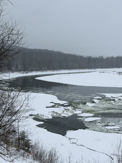 Frozen river with ice chunks along snowy banks and forested hills in winter
