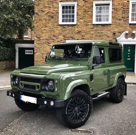 Green off-road SUV parked on a street beside a brick building