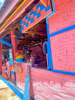 Colorful pink and blue woven bamboo beach bar with tropical fruits displayed inside