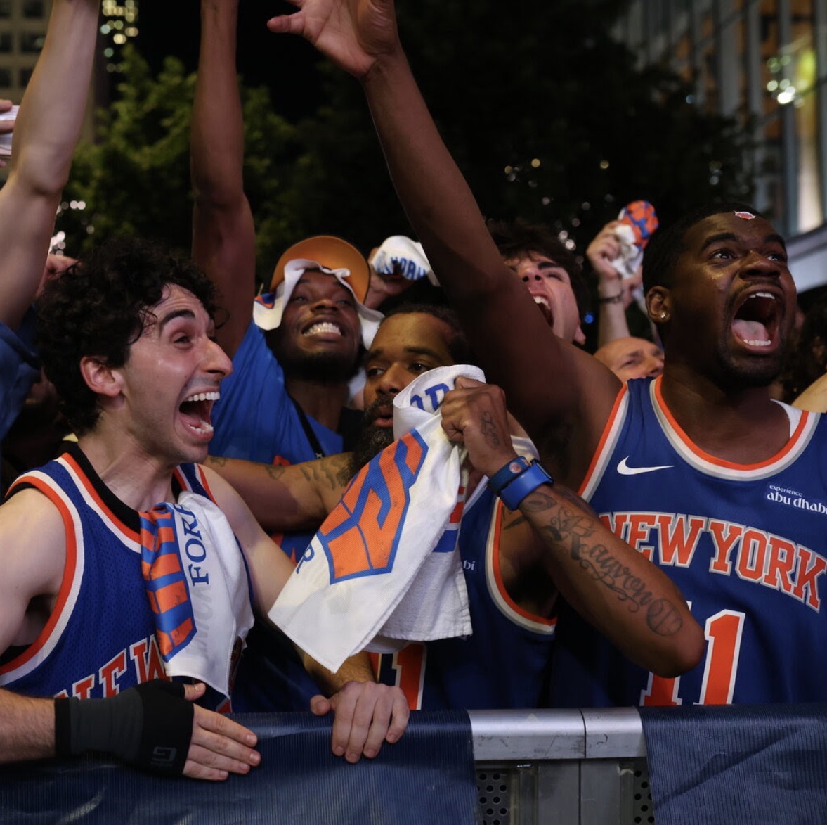 Cheering New York Knicks fans in blue jerseys at a nighttime game celebration