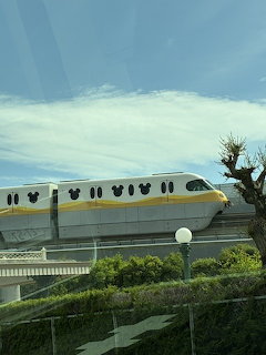 Yellow and white Disney monorail on elevated track with cloudy sky and green landscaping