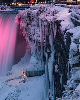 Frozen Niagara Falls at night with pink lights illuminating ice-covered cliffs and cascading water