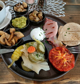 Assorted breakfast foods including eggs, tomato, ham, bread, and sides on black plates