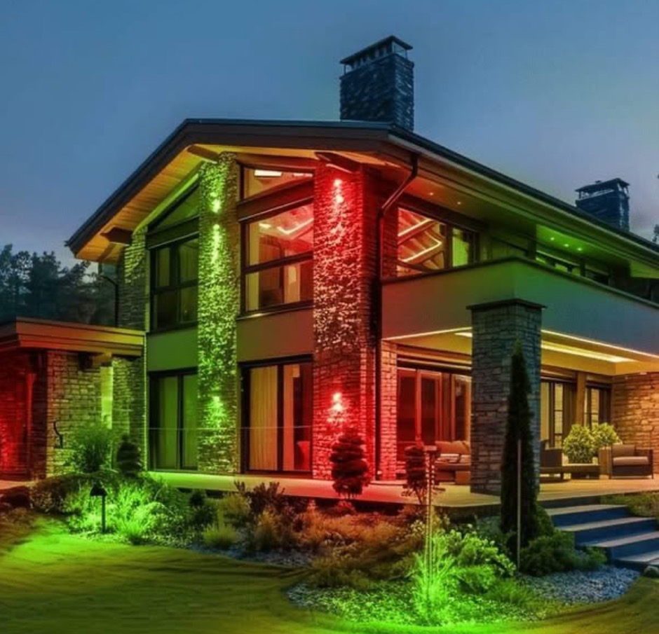 Modern house at dusk with red and green lights, stone columns, and landscaped yard