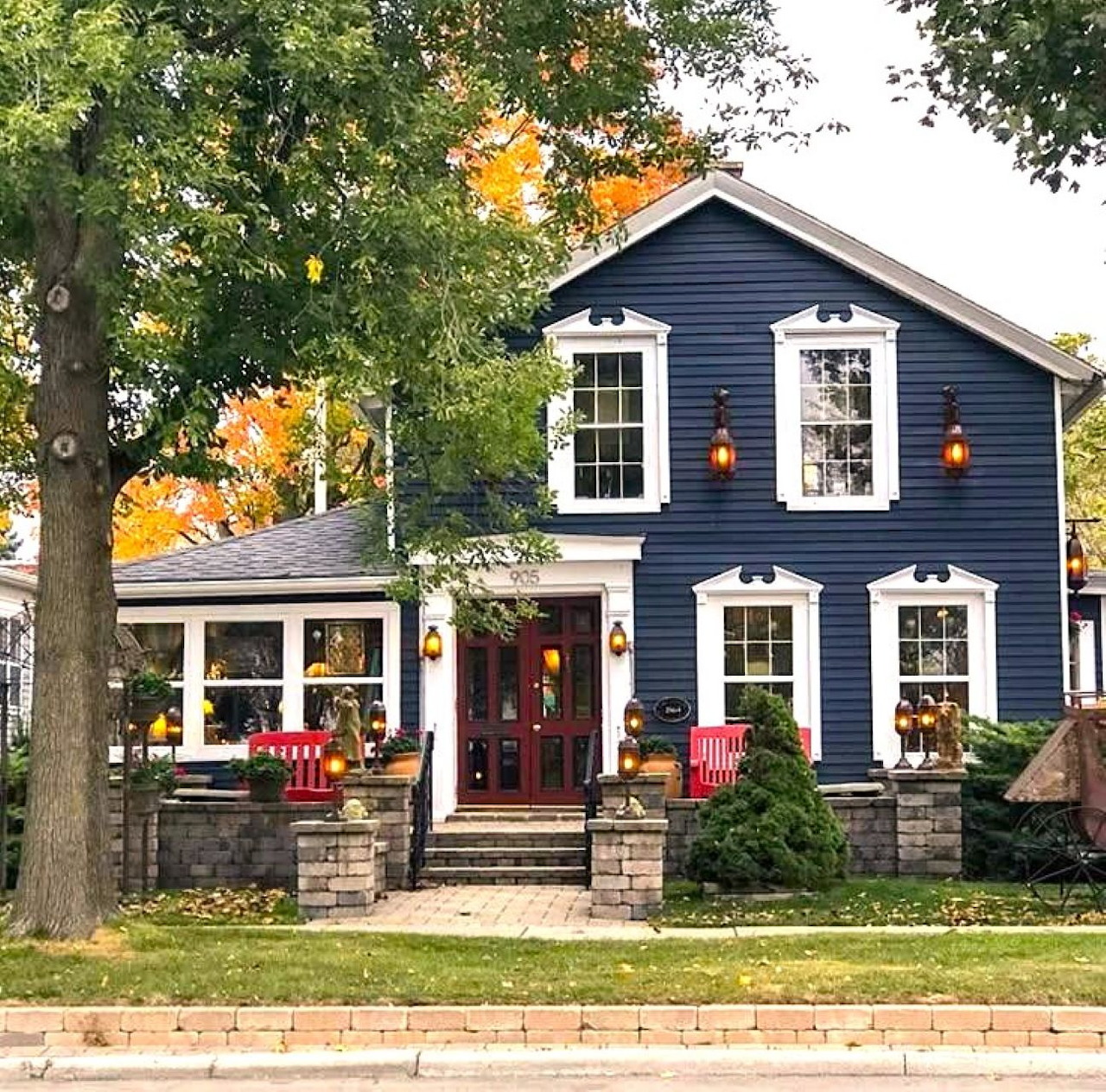Blue two-story house with white trim, red front door, stone porch, and large trees