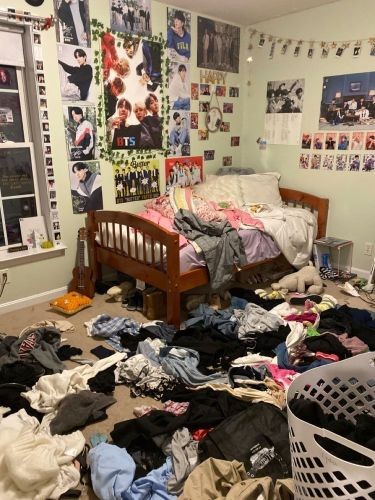 Messy bedroom with clothes on floor, wooden bed, and poster-covered walls