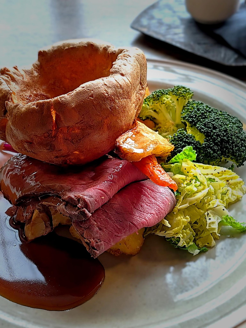 Plate of roast beef with Yorkshire pudding, gravy, broccoli, cabbage, and roasted vegetables