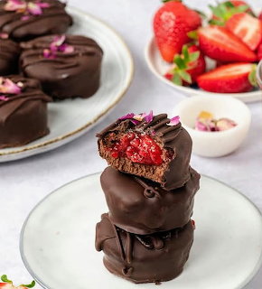 Stack of chocolate-covered treats with strawberry filling on a white plate with strawberries in background