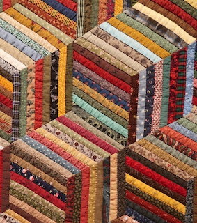 Hexagonal log cabin quilt pattern with multicolored fabric strips in warm earthy tones