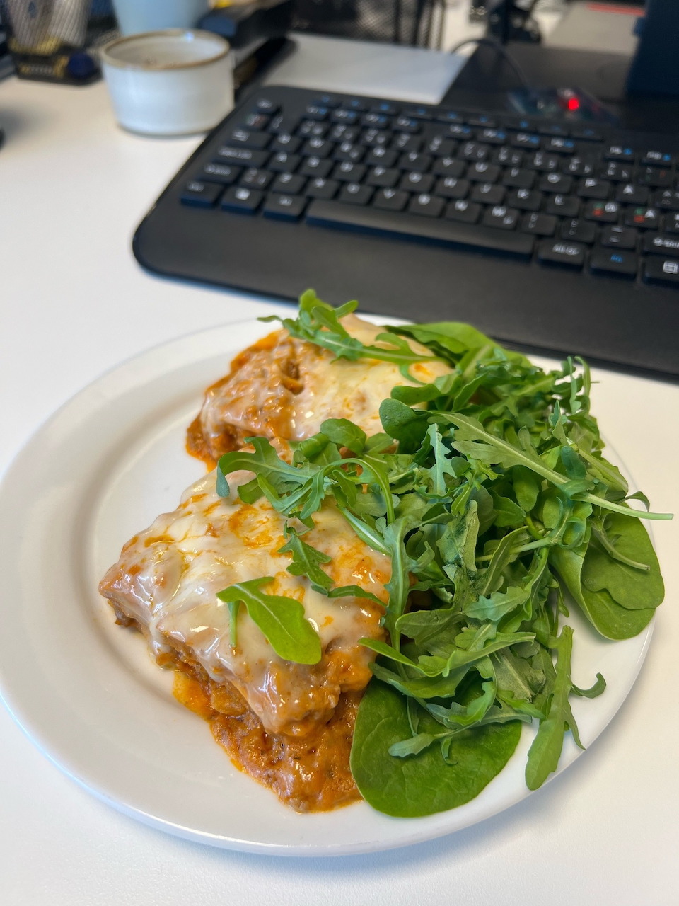 White plate with a slice of cheesy lasagna in tomato sauce and a side of fresh green arugula and spinach salad