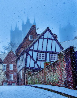 Snow-covered half-timbered house with Lincoln Cathedral spires visible through fog in background