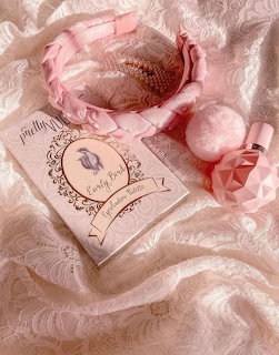 Pink headband, pom-pom, perfume bottle and book on pink lace background
