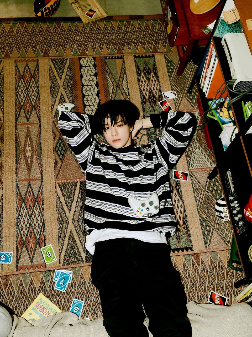 Young man in striped sweater lying on a geometric patterned rug with scattered cards around him