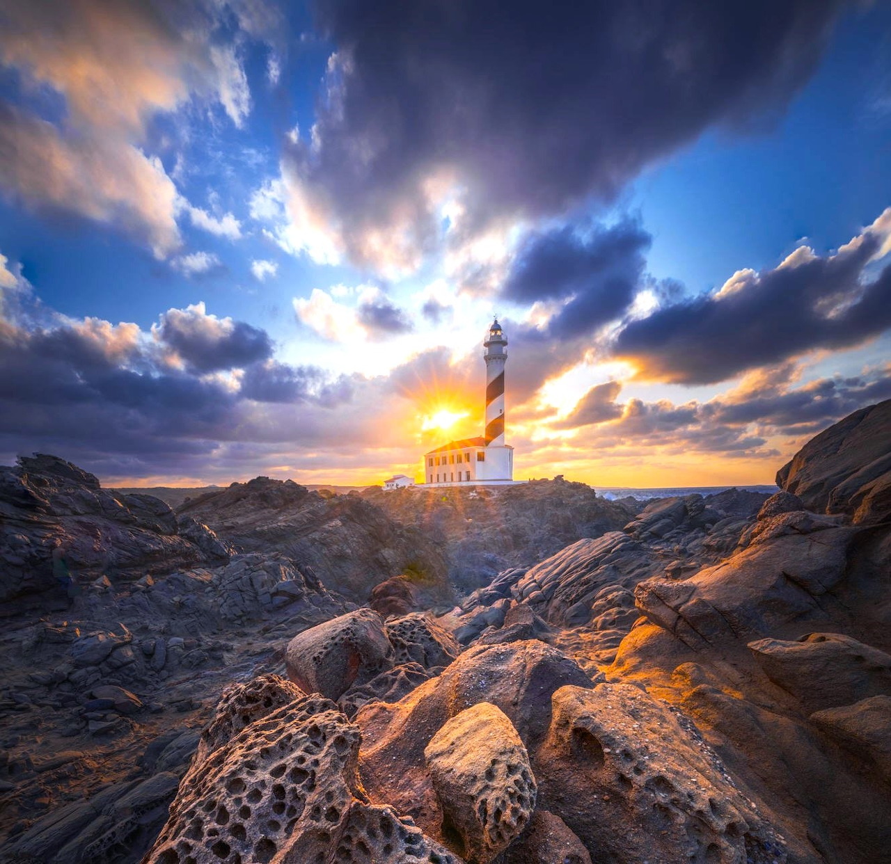 White lighthouse on rocky coast at sunset with dramatic cloudy sky