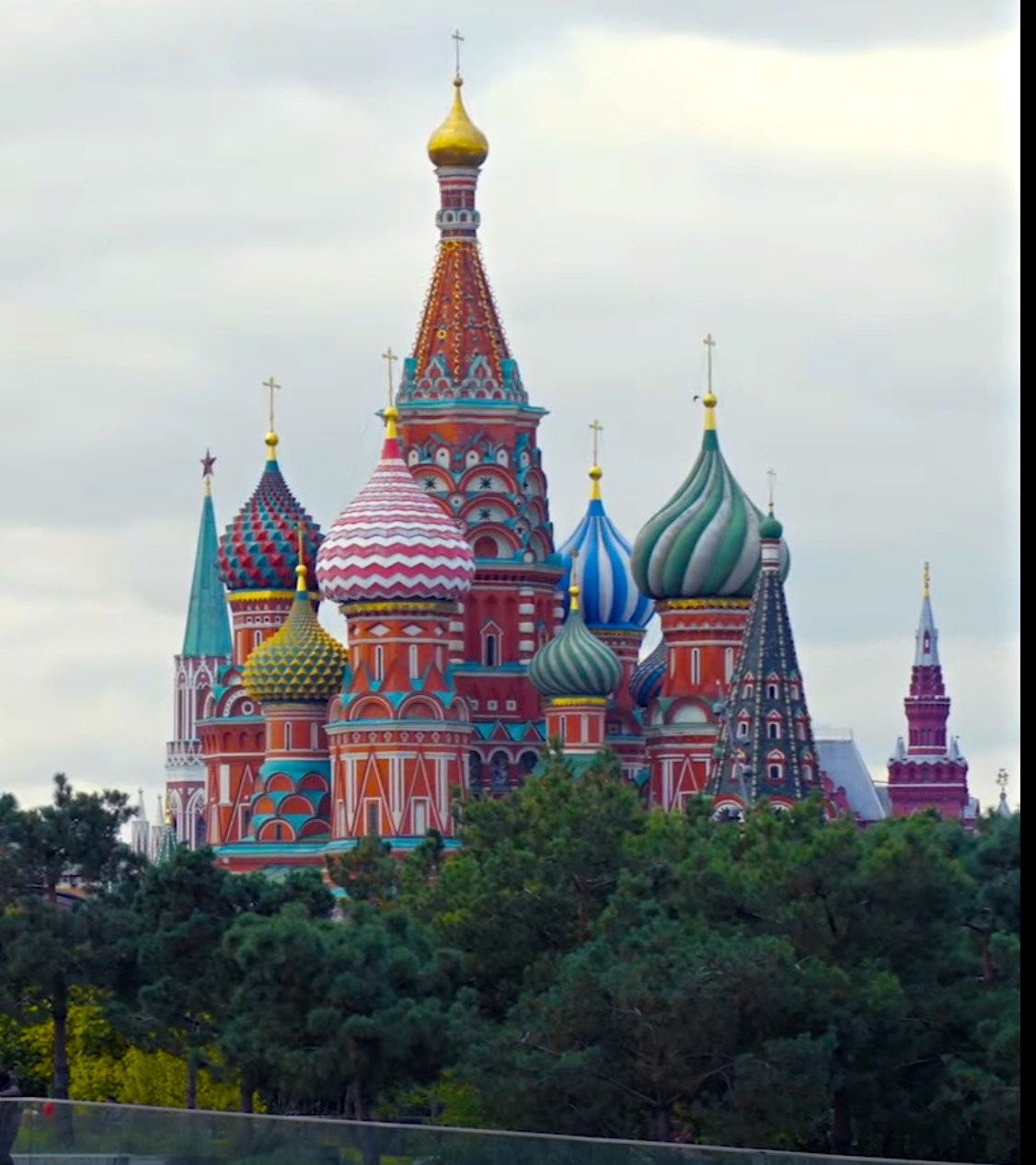 Saint Basil's Cathedral in Moscow with colorful onion domes and Kremlin tower behind green trees