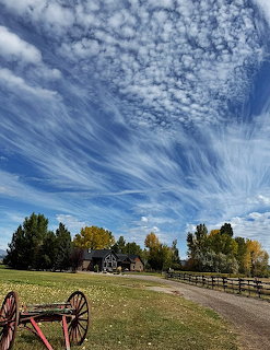 Rural field with a farmhouse, wooden fence, wagon wheel, and dramatic cloud-filled blue sky