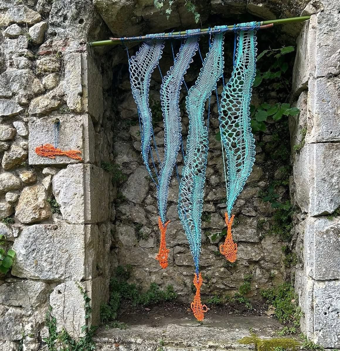 Blue lace fish hang in a stone window opening framed by an old rustic wall.