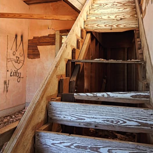 Old wooden staircase inside an abandoned building with wall graffiti and debris